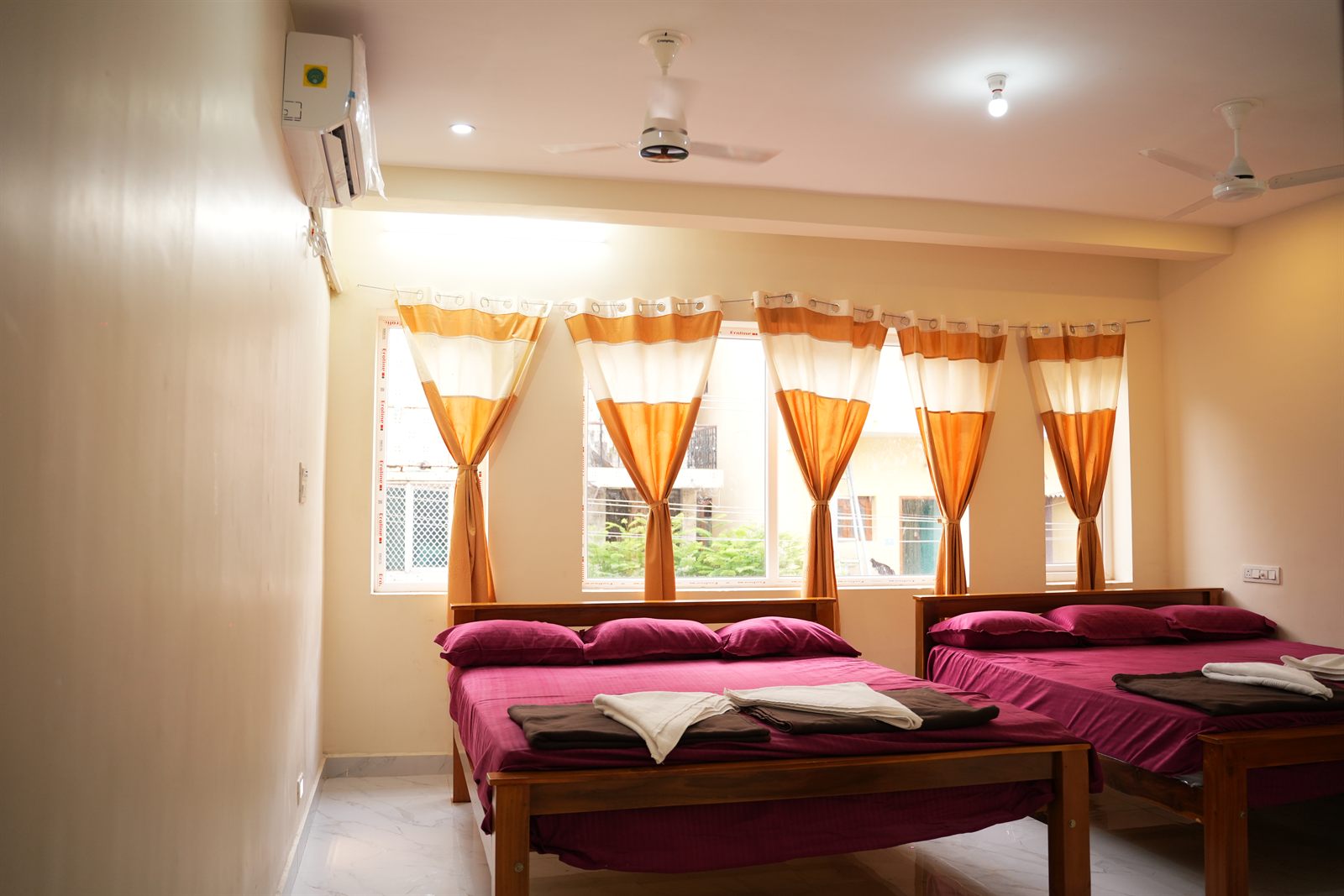 Spacious family room with multiple beds, orange curtains and natural light
