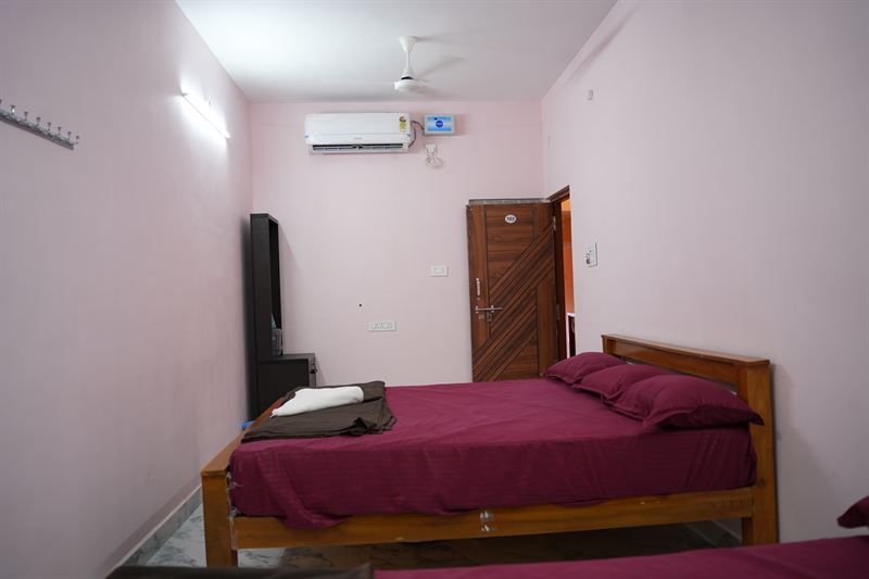 Standard non-AC room with pink walls, wooden bed, TV cabinet and dressing mirror